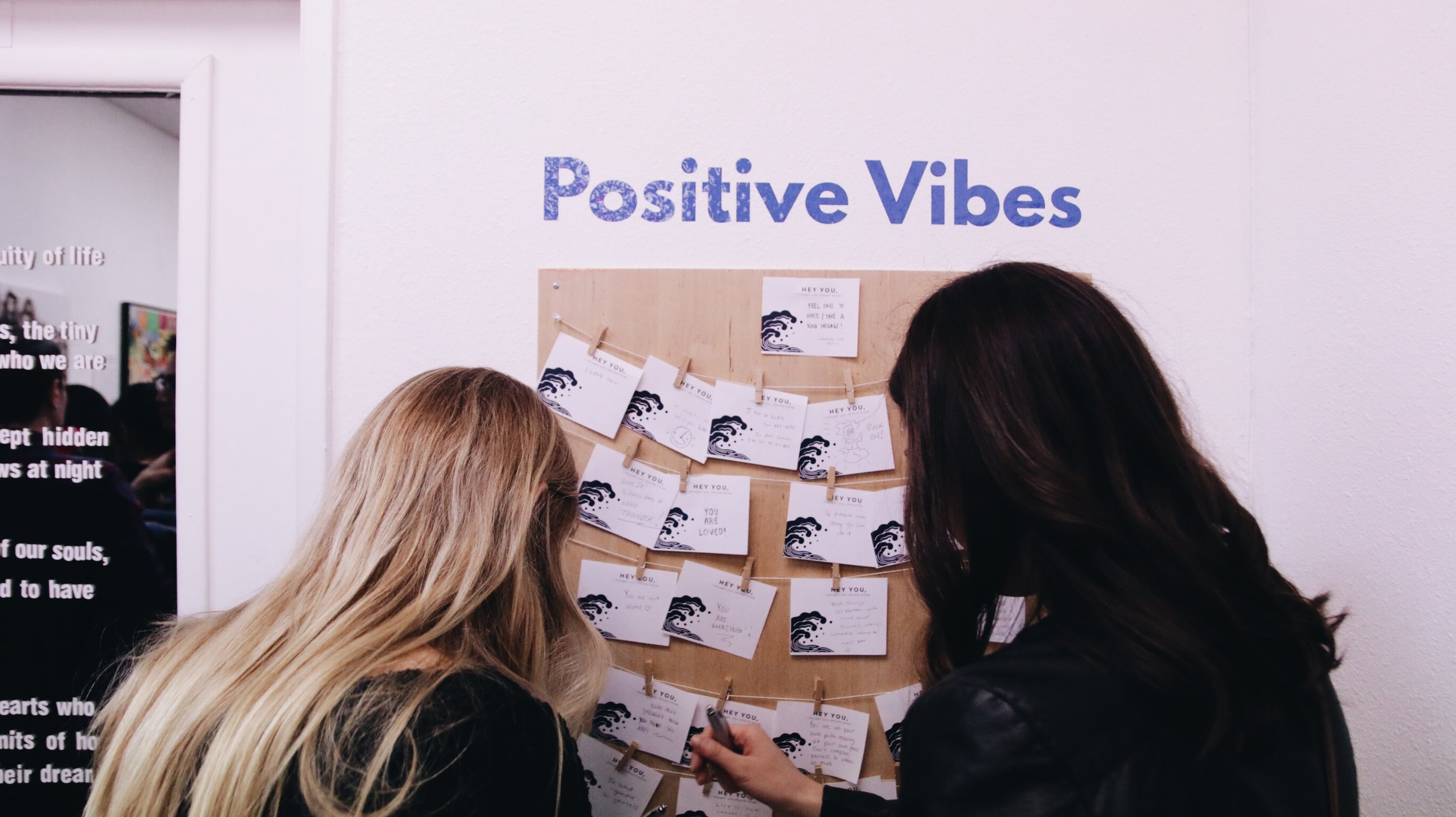 Two women post “Positive Vibes” on a board for others to read. 