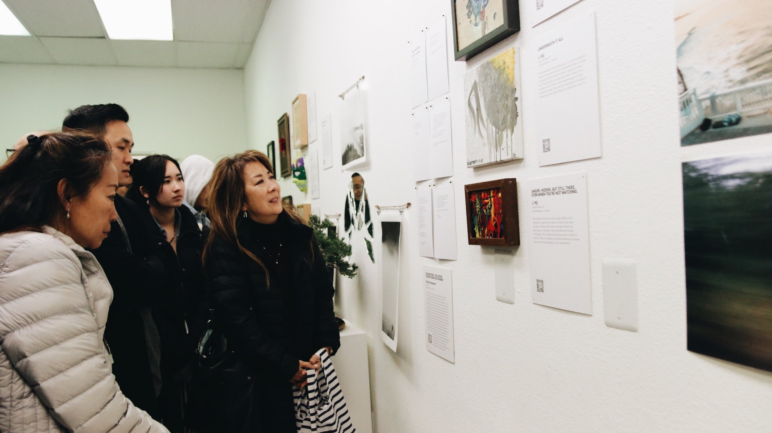 A small group gathers as they look at artwork on the wall. 