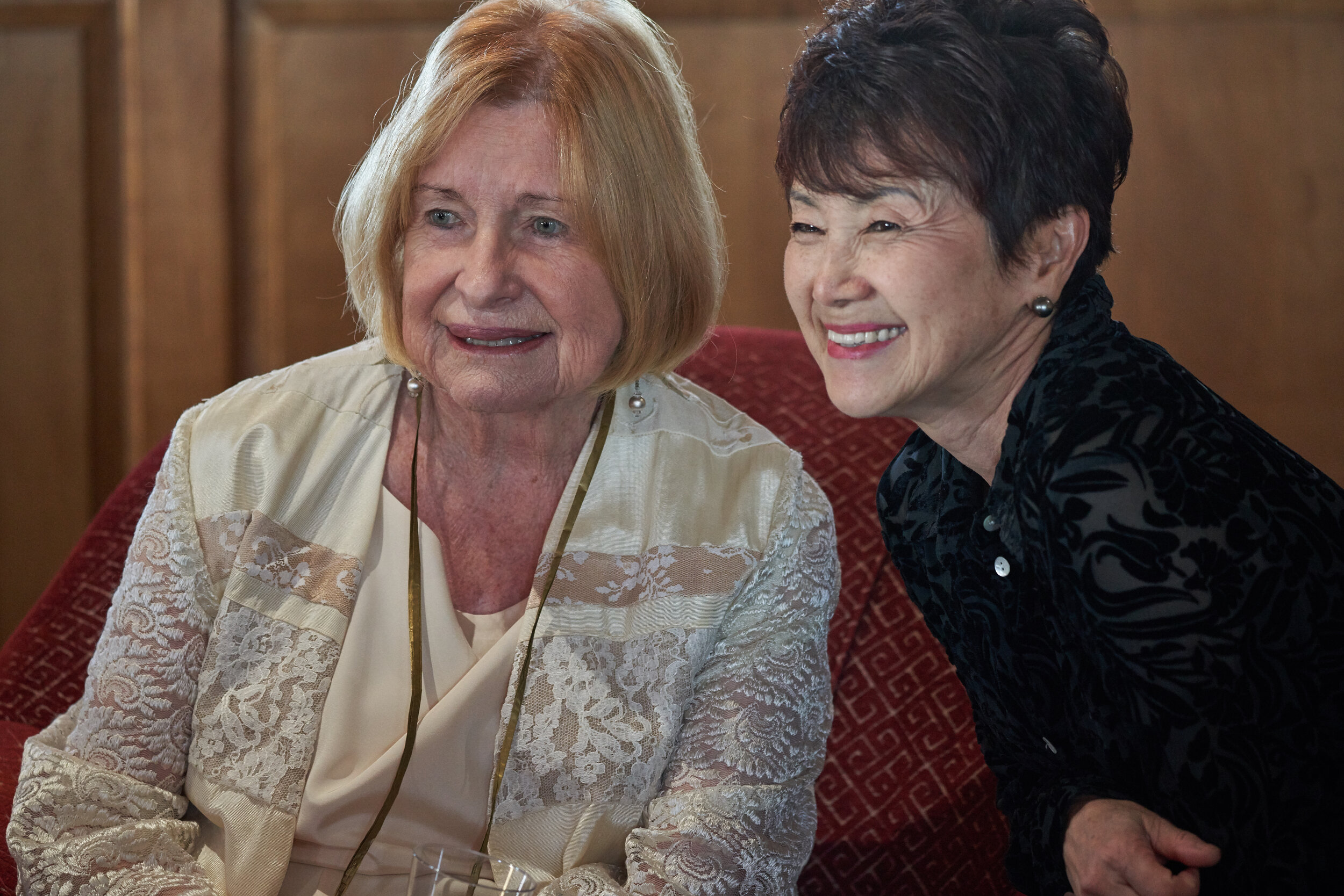 Two women smile while seated inside. 