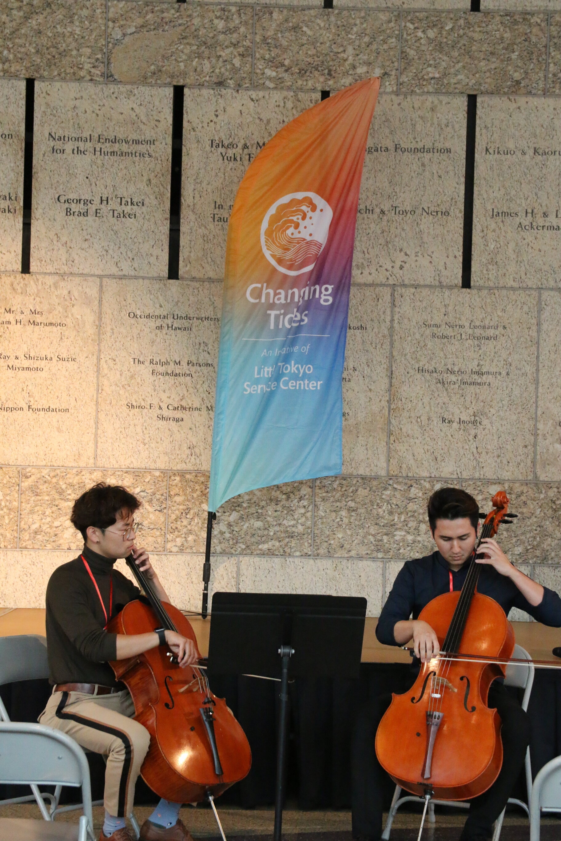 Two men play the cello. 