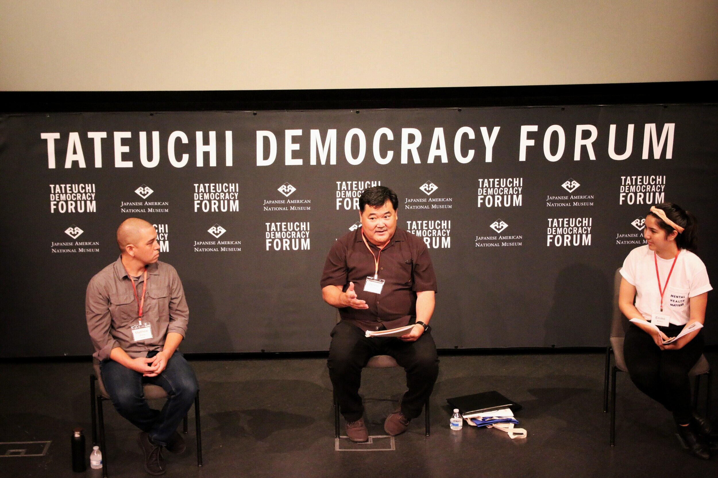 A man speaks in front of a sign that says “Japanese American National Museum” and “Tateuchi Democracy Forum.”  