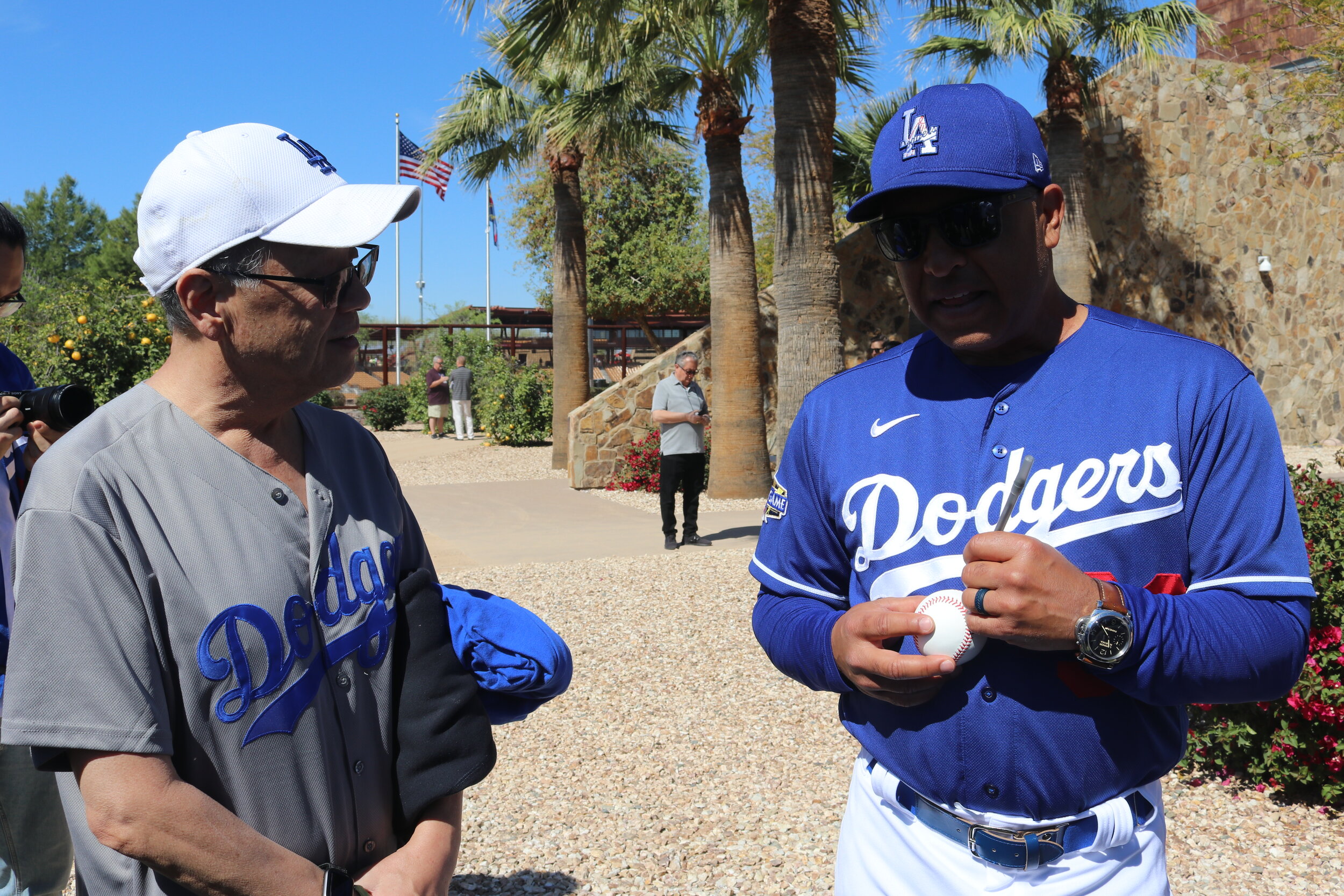 A man wearing a Dodgers jersey signs a ball for an older gentleman. 