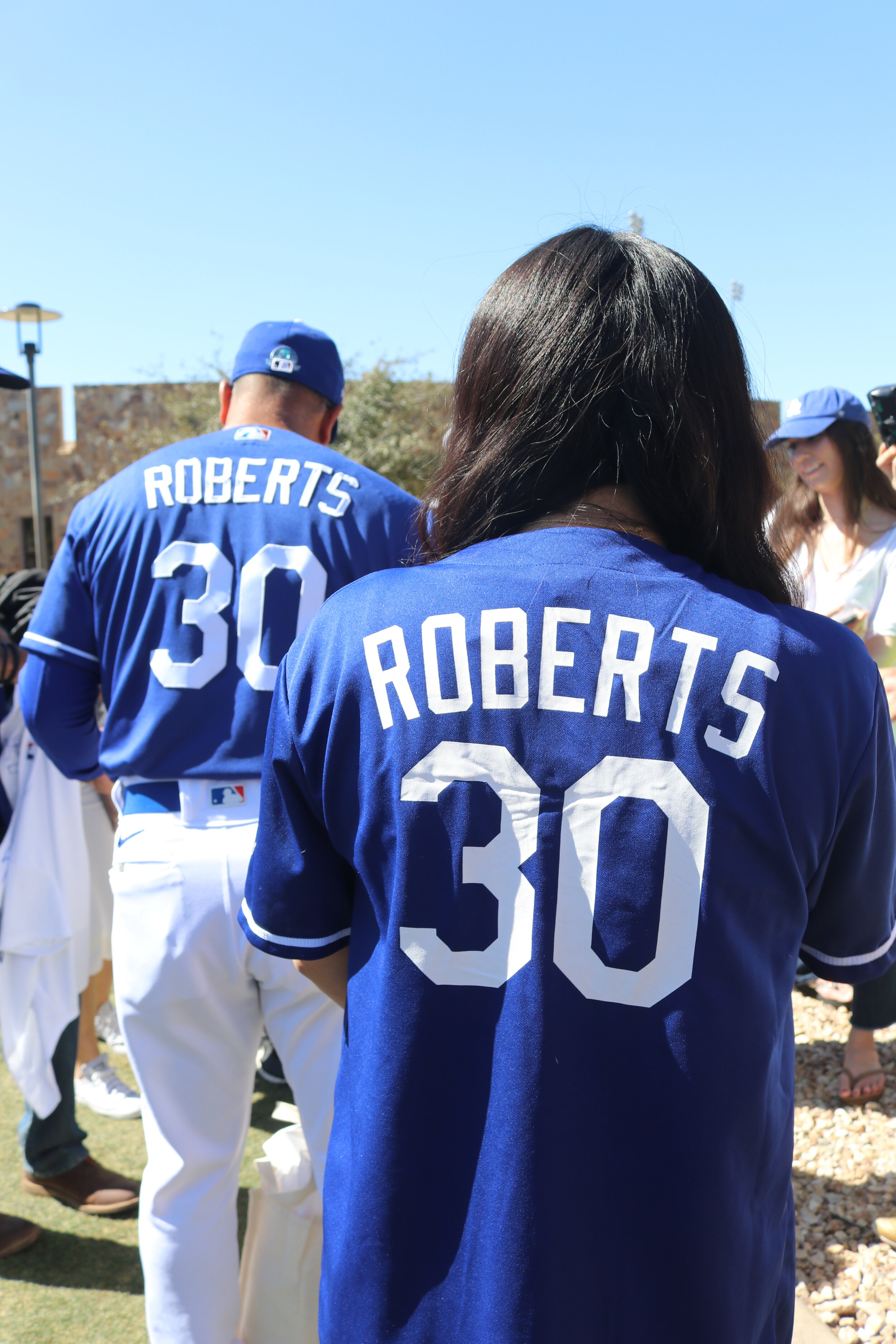 A fan wearing a Roberts Dodger jersey stands behind baseball player Roberts who is also wearing his uniform with his name on it. 