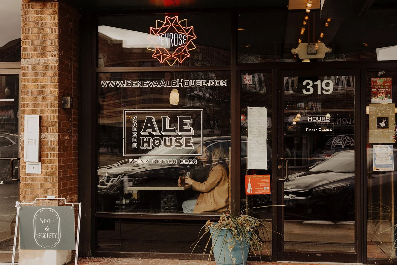 A couple is photographed through the front glass of Geneva Ale House during engagement photography in Geneva IL