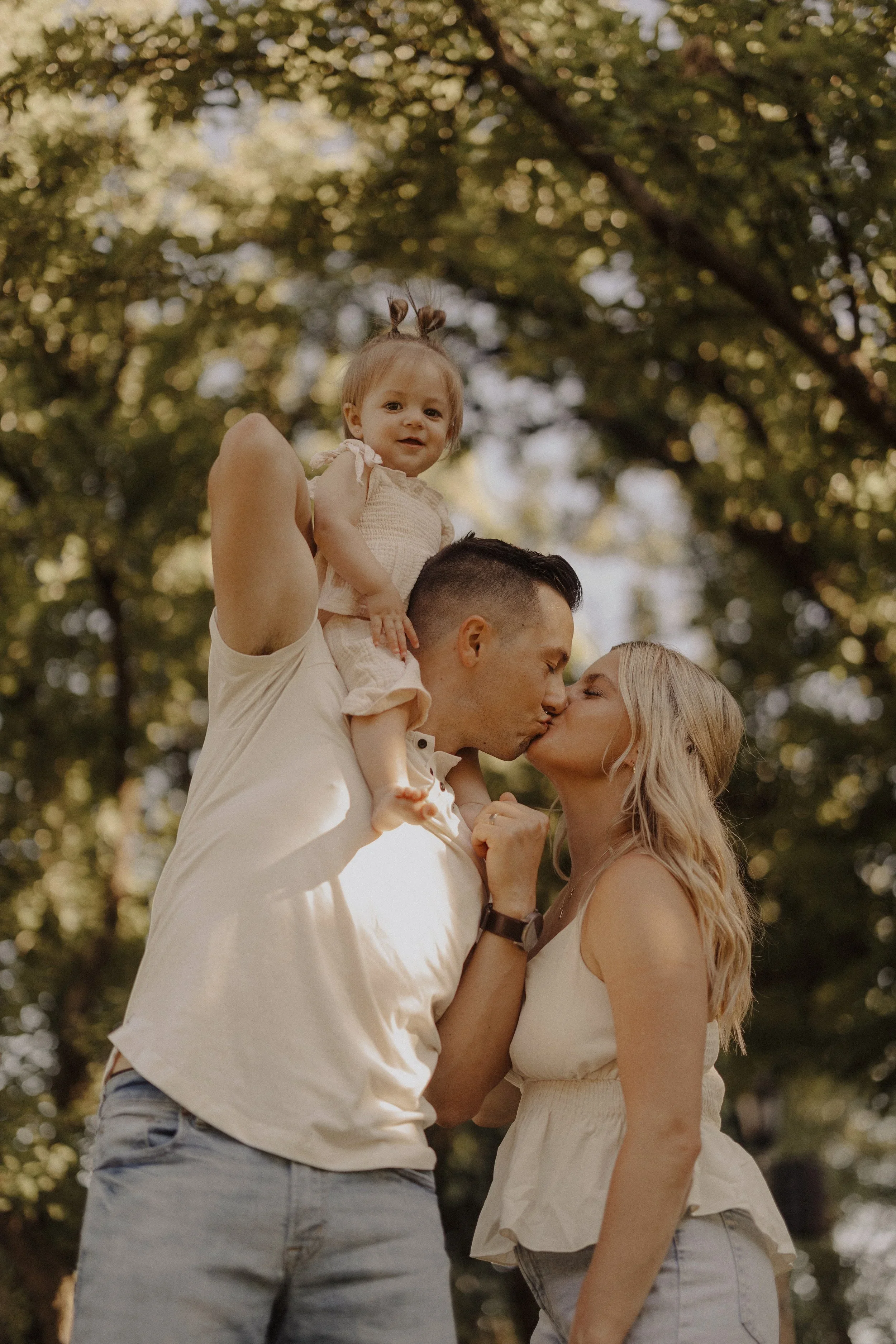 Parents kissing while holding baby during outdoor family session by Chicago photographer
