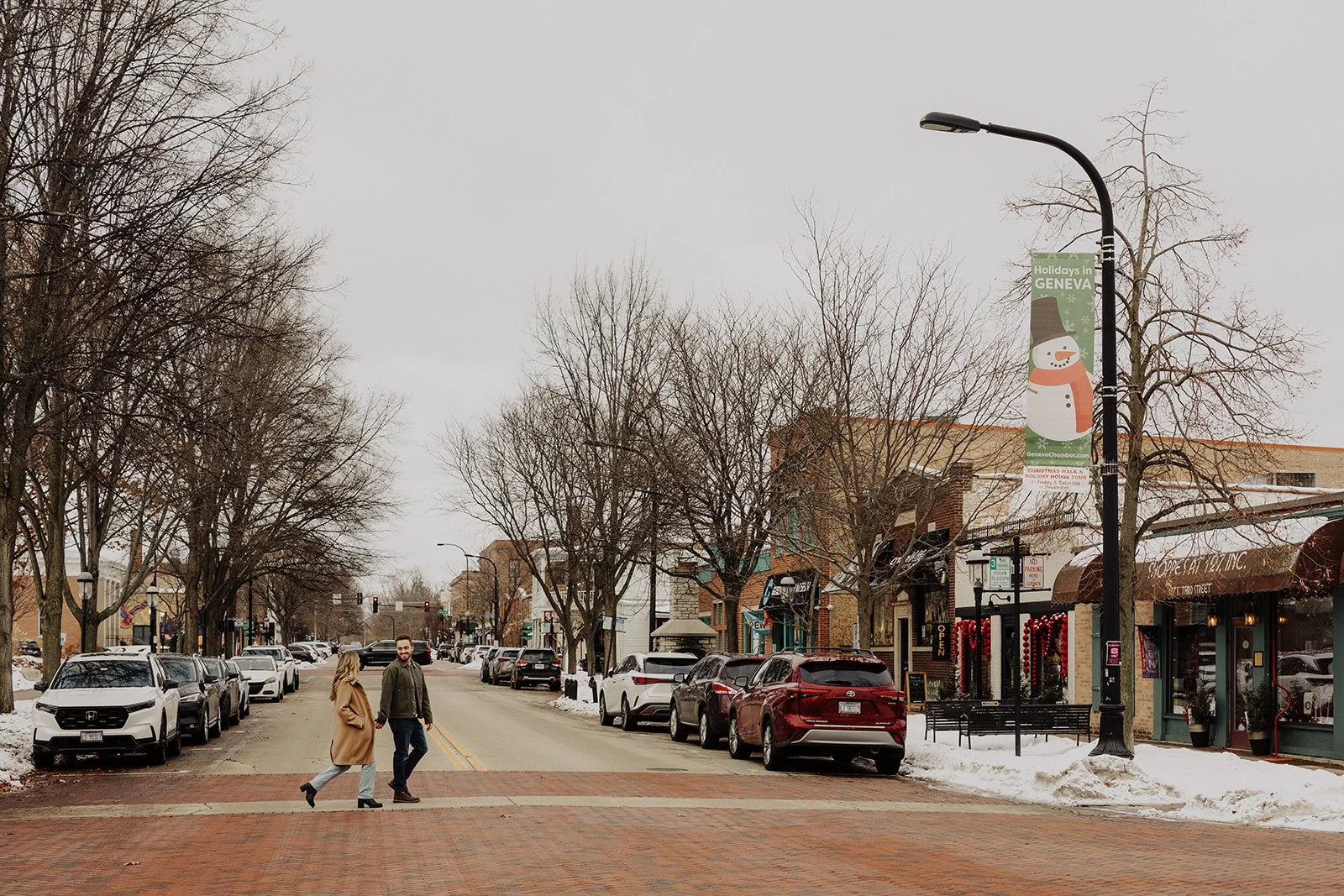 An engaged couple holds hands as they cross the street downtown during engagement photography in Geneva IL