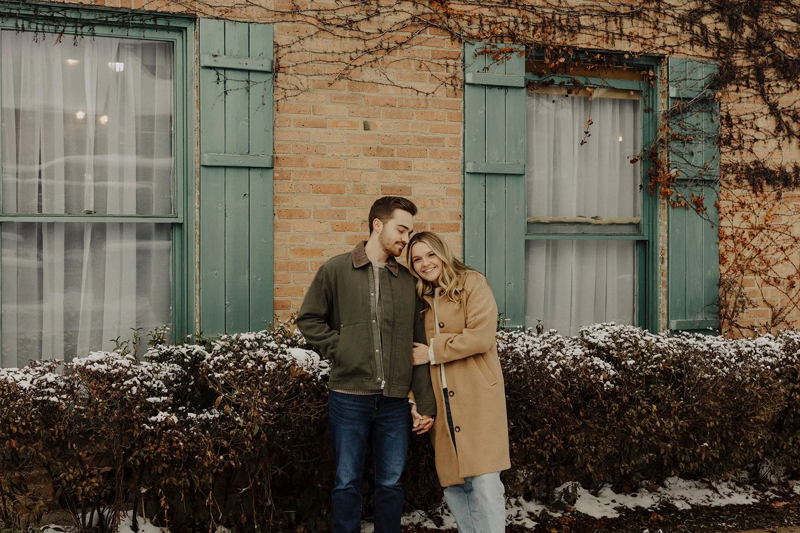 A  couple snuggle up in winter coats during a snowy winter engagement photography in Geneva Il