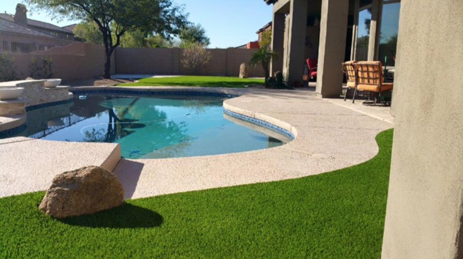  Artificial grass installation next to pool with boulders inset  