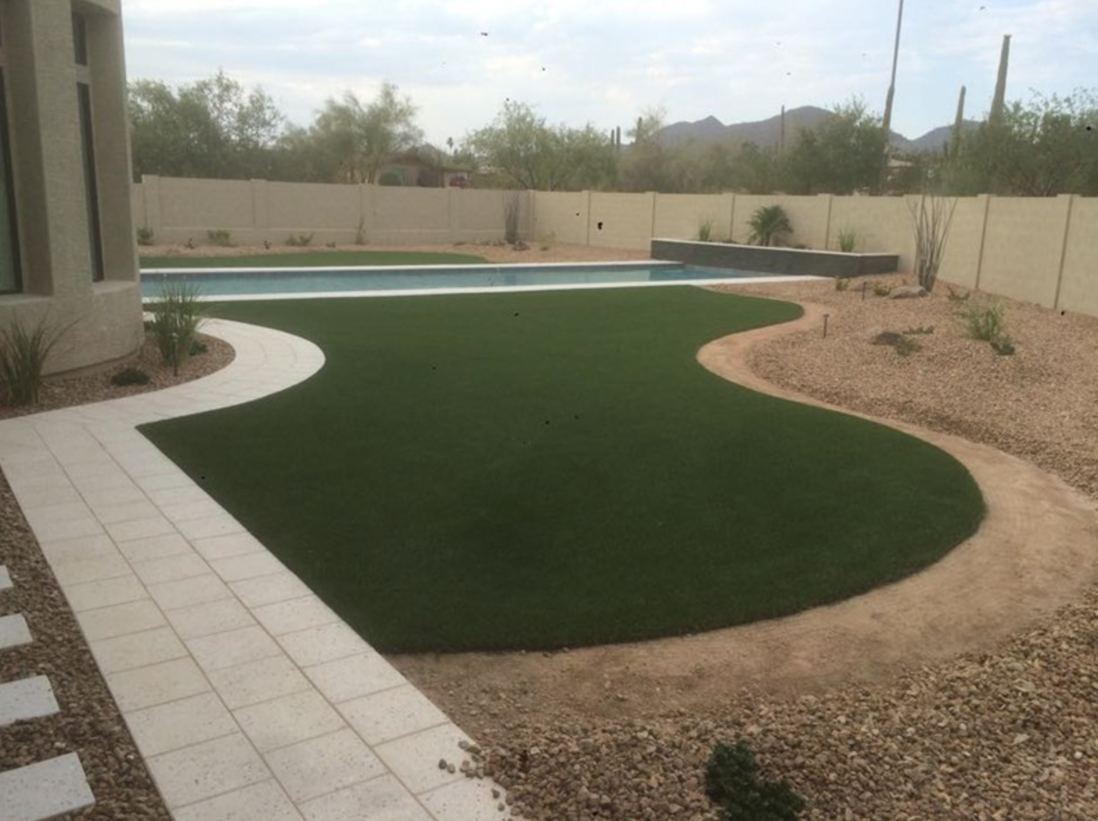  Artificial grass installation next too pool with curved lines and paver walkway. 