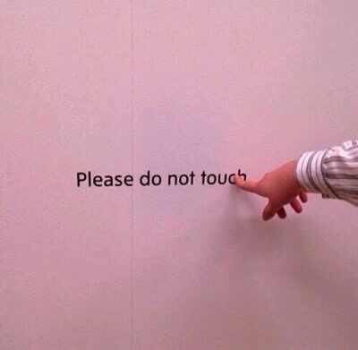 A photo of a finger pointing at words on a wall that say, “Please do not touch.”