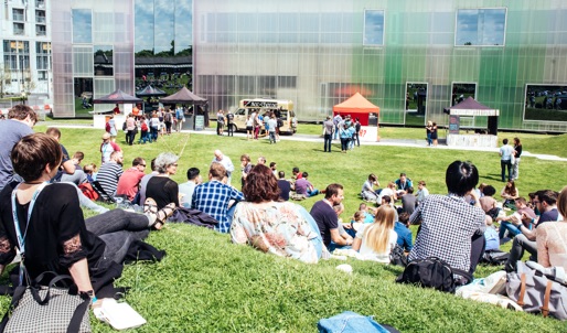 A photo of groups of people sitting outside on a grassy area right next to a large building.