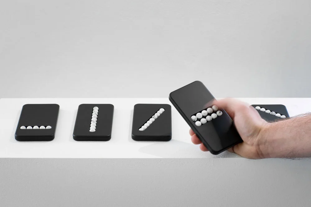 A photo of four substitute phones laying on a table and one in a person’s hand. Each is a solid piece except where there are rolling balls someone could slide their finger over.