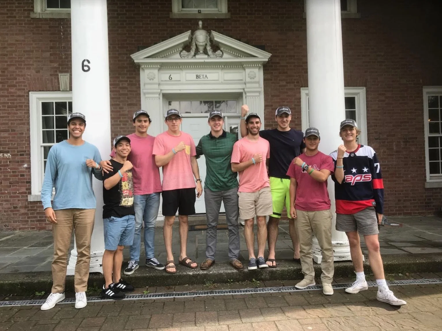 A group of college students standing in front of a fraternity house wearing hats that say “Mindhood” on them.