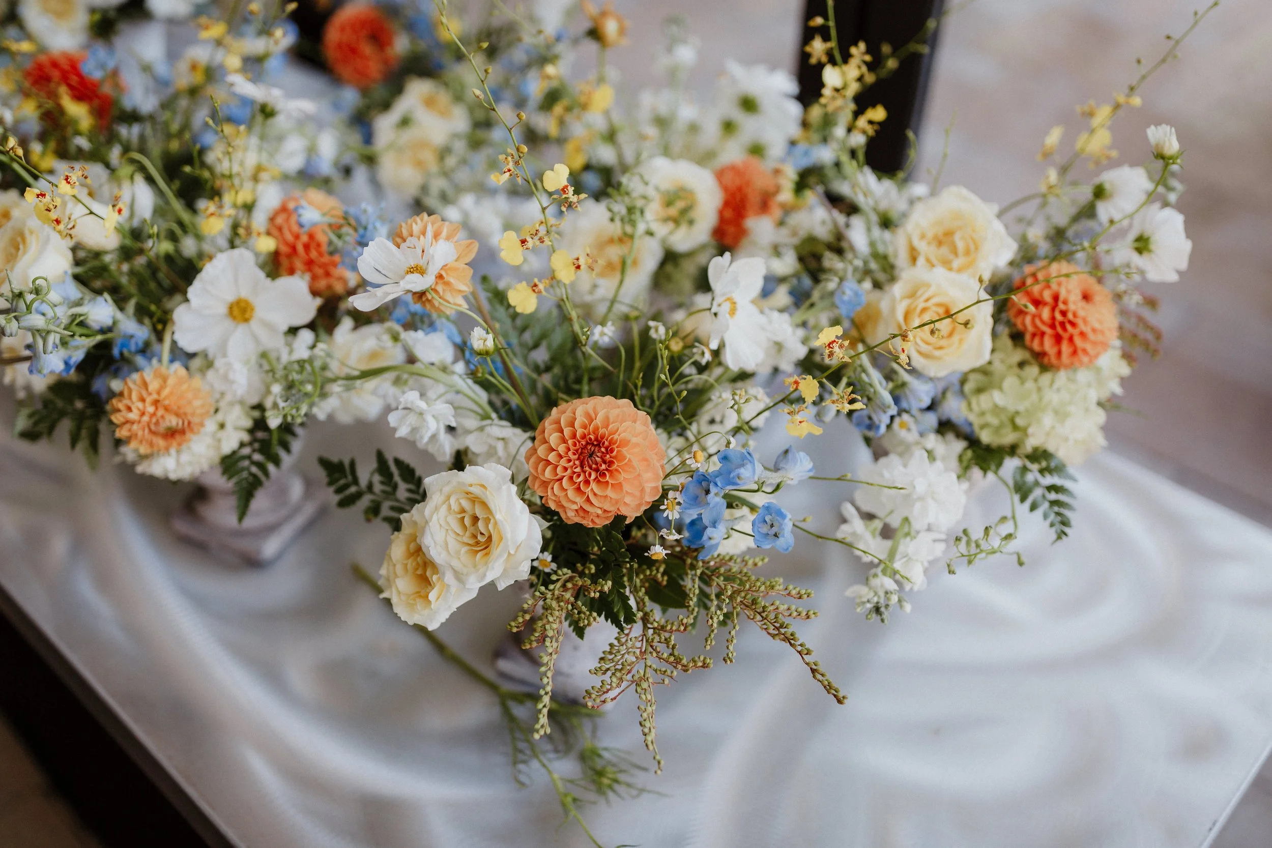 Whimsical floral arrangement of locally sourced dahlias with cosmos, oncidium orchids, delphinium, spray roses and pieris japonica