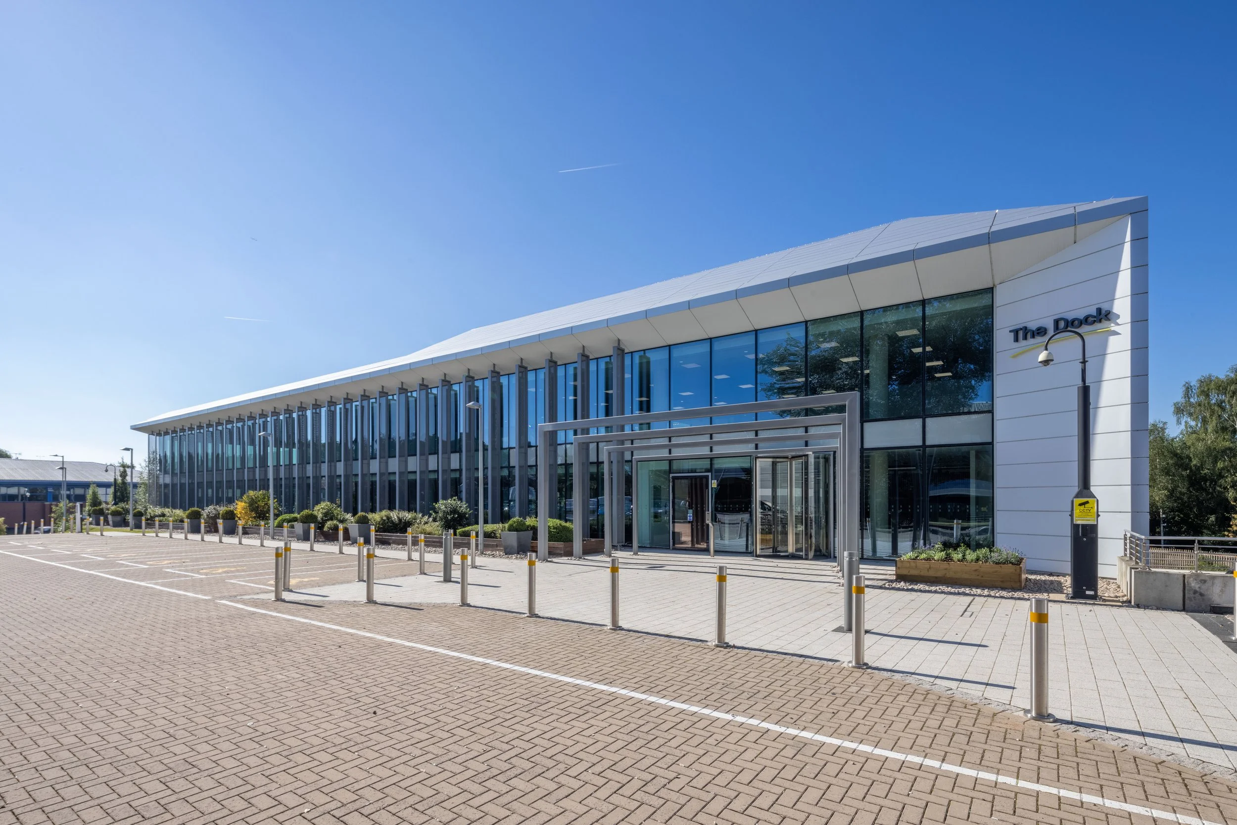 Modern office building with glass facade, labeled 'The Dock', under a clear blue sky.