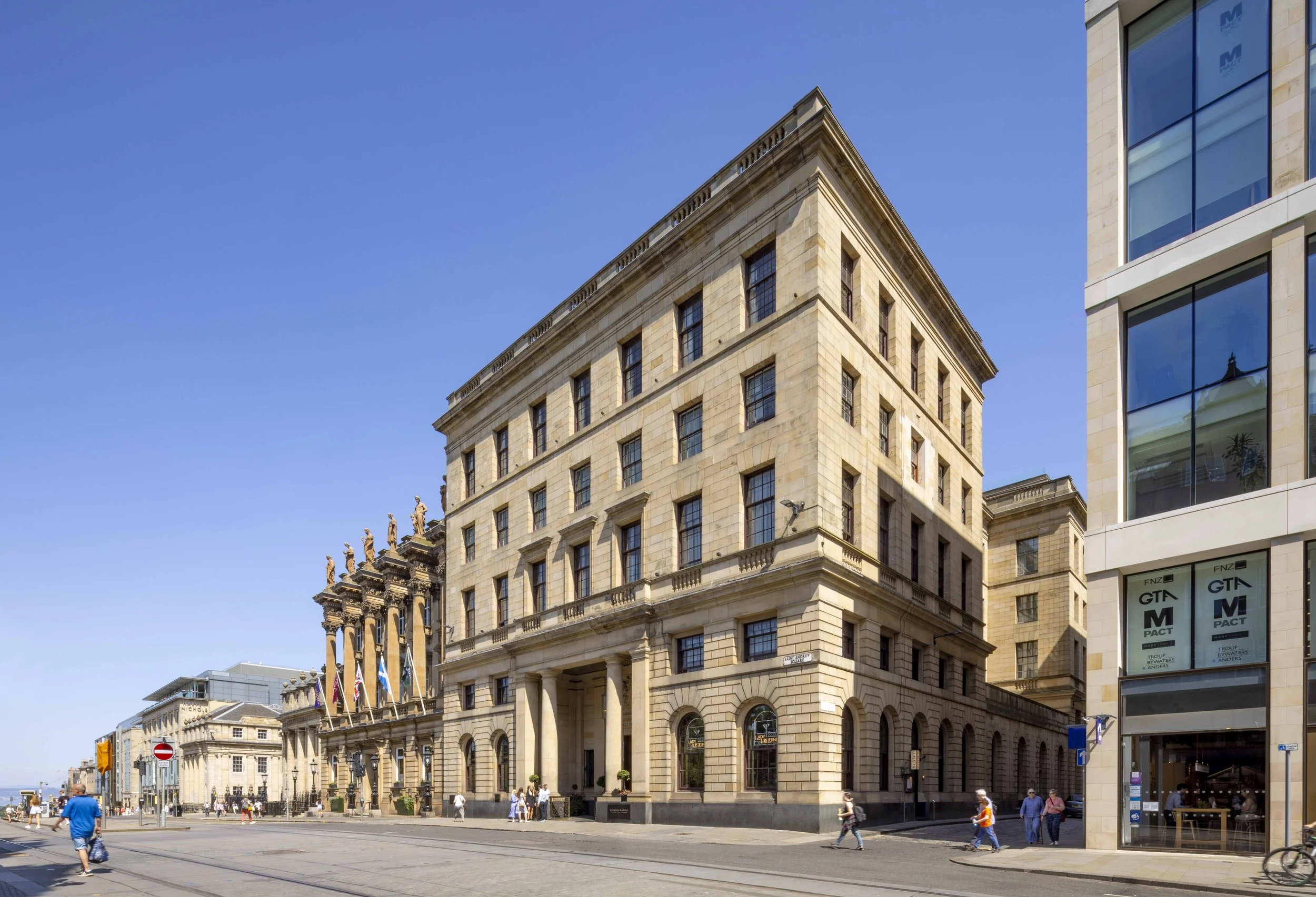 Exterior view of a historic building with columns and statues, located on a city street under a clear blue sky.