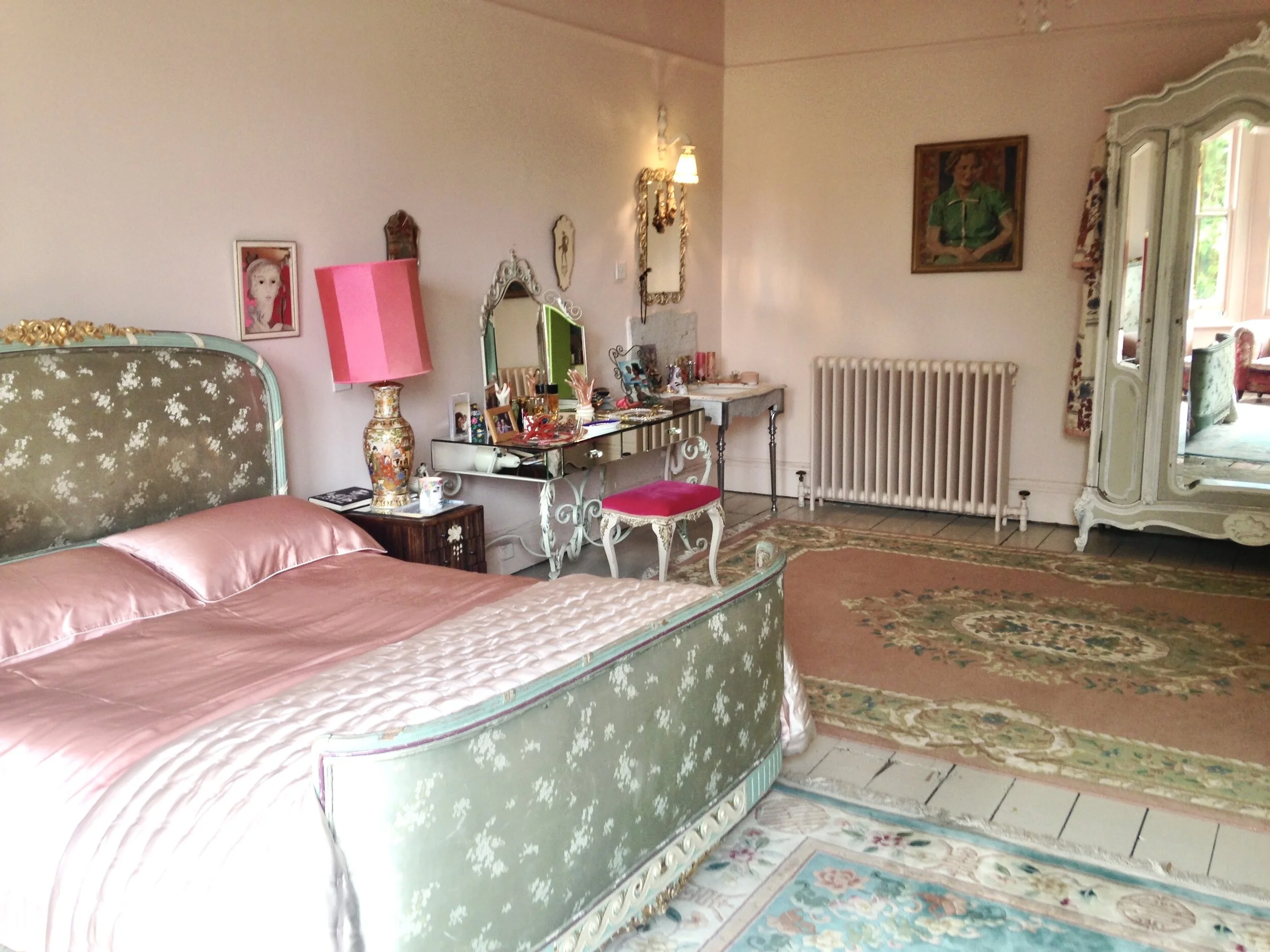 French bed, tick, upholstered in patterned silk, tick, with contrasting vintage rugs, tick, with satin bedding, tick, with mirrored amoire, tick. Marianne Cotterrill does it again.