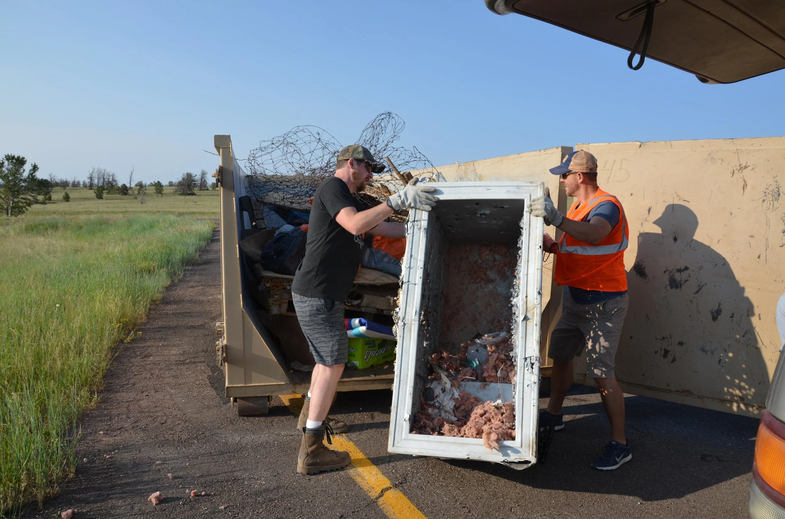 Volunteers move a discarded refrigerator into a dumpster during the 2018 Pole Mountain Cleanup. (Photo by Willow Belden)