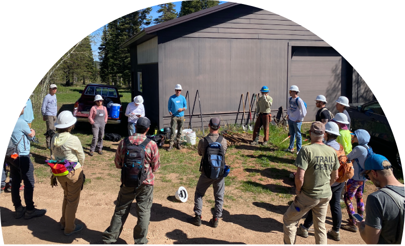 Group of people with hardhats in a circle by a large shed outside