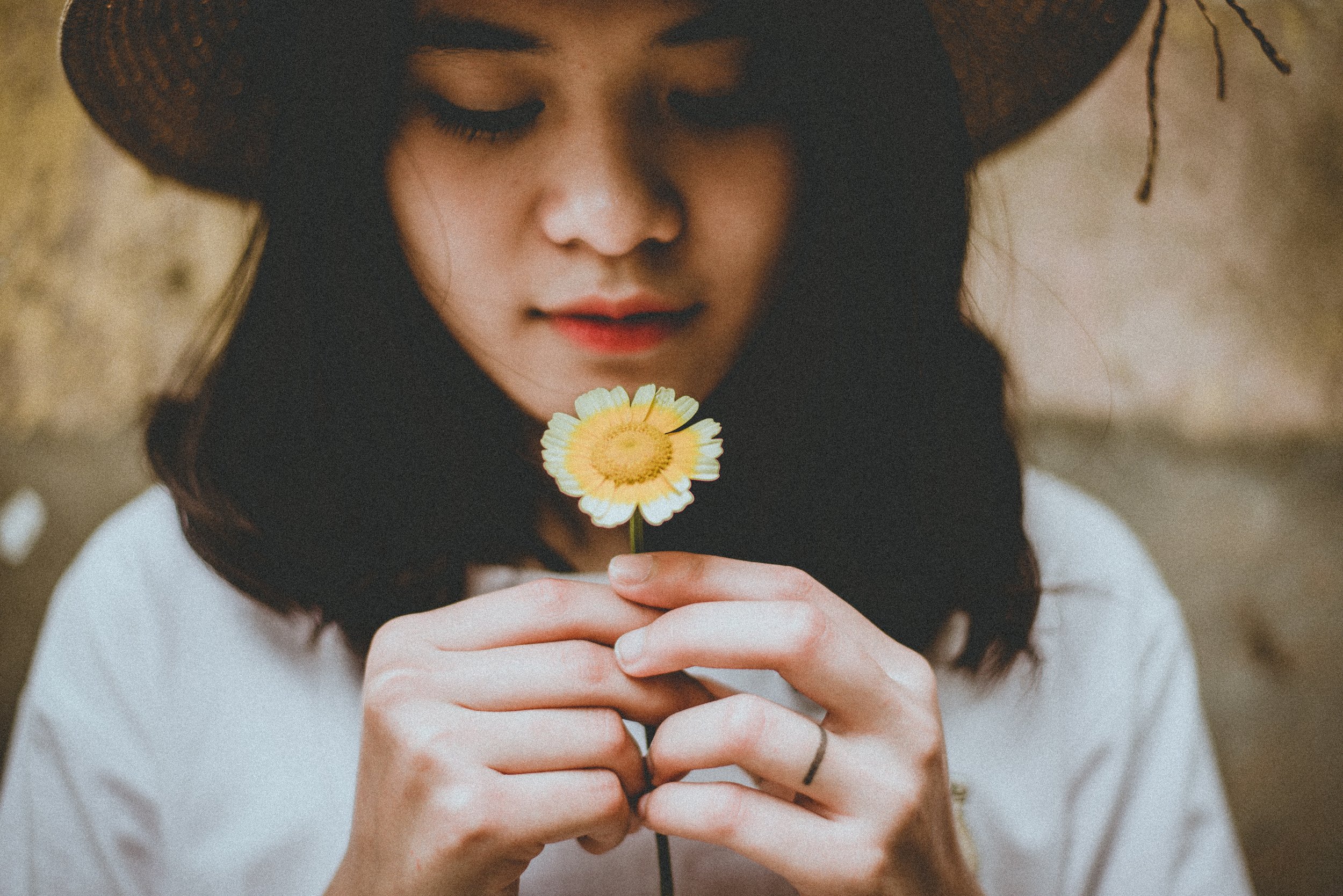 A grieving teen girl holds a daisy in her hands. Her gaze is focused down toward the flower.