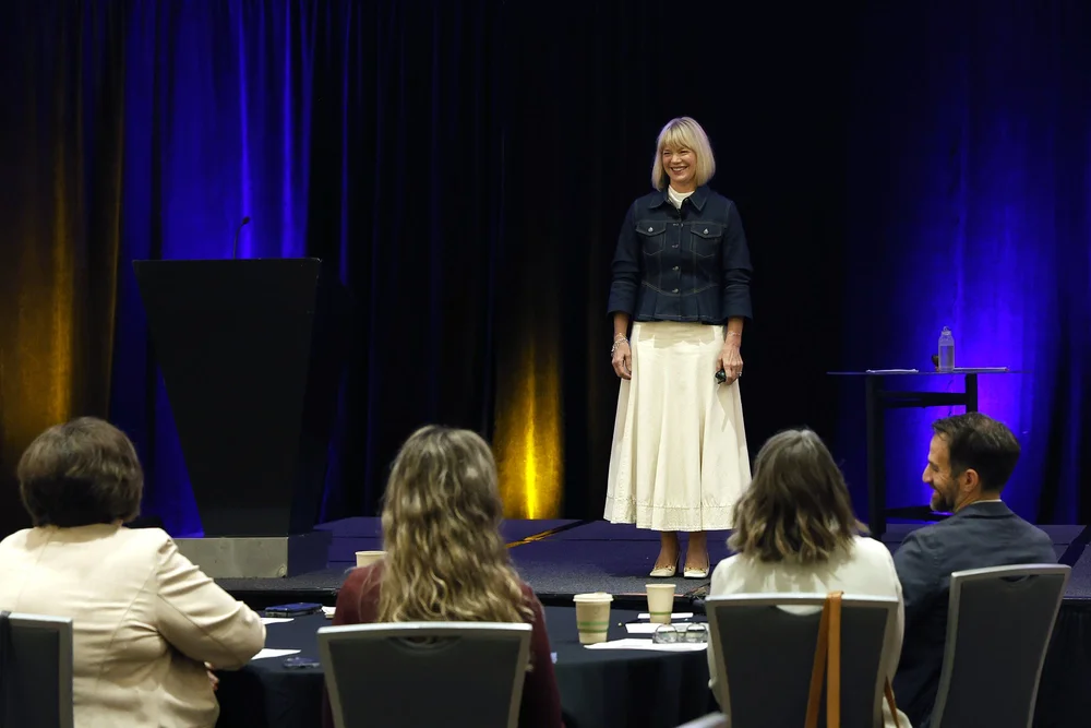 Ashley Nelson speaking into a microphone and gesturing to an audience
