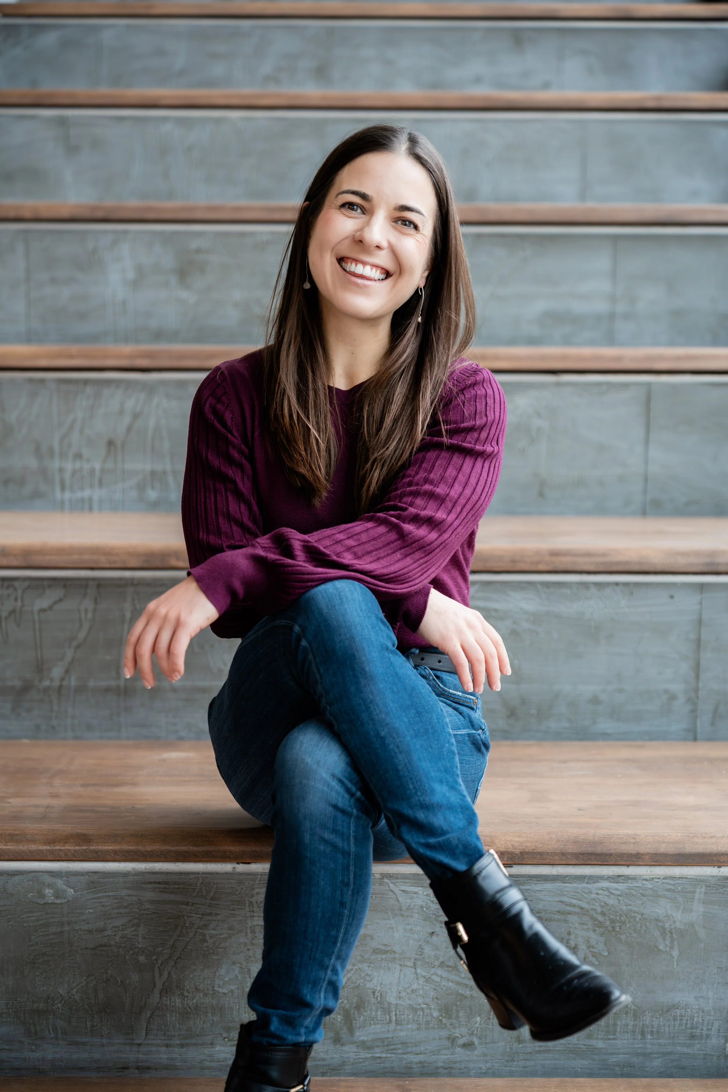 Woman sitting on stairs, wearing purple sweater and jeans