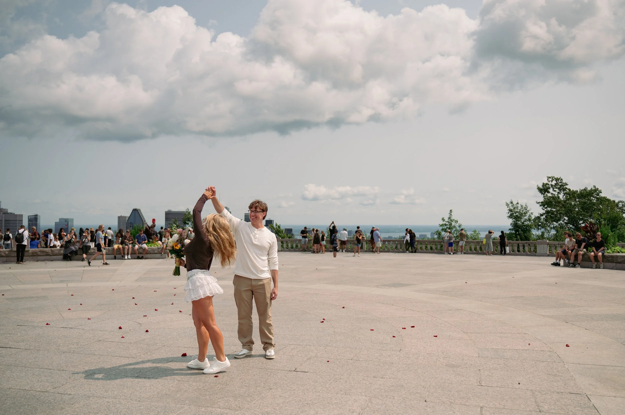 A man twirls a woman around on the mountain summit, with people all around. 