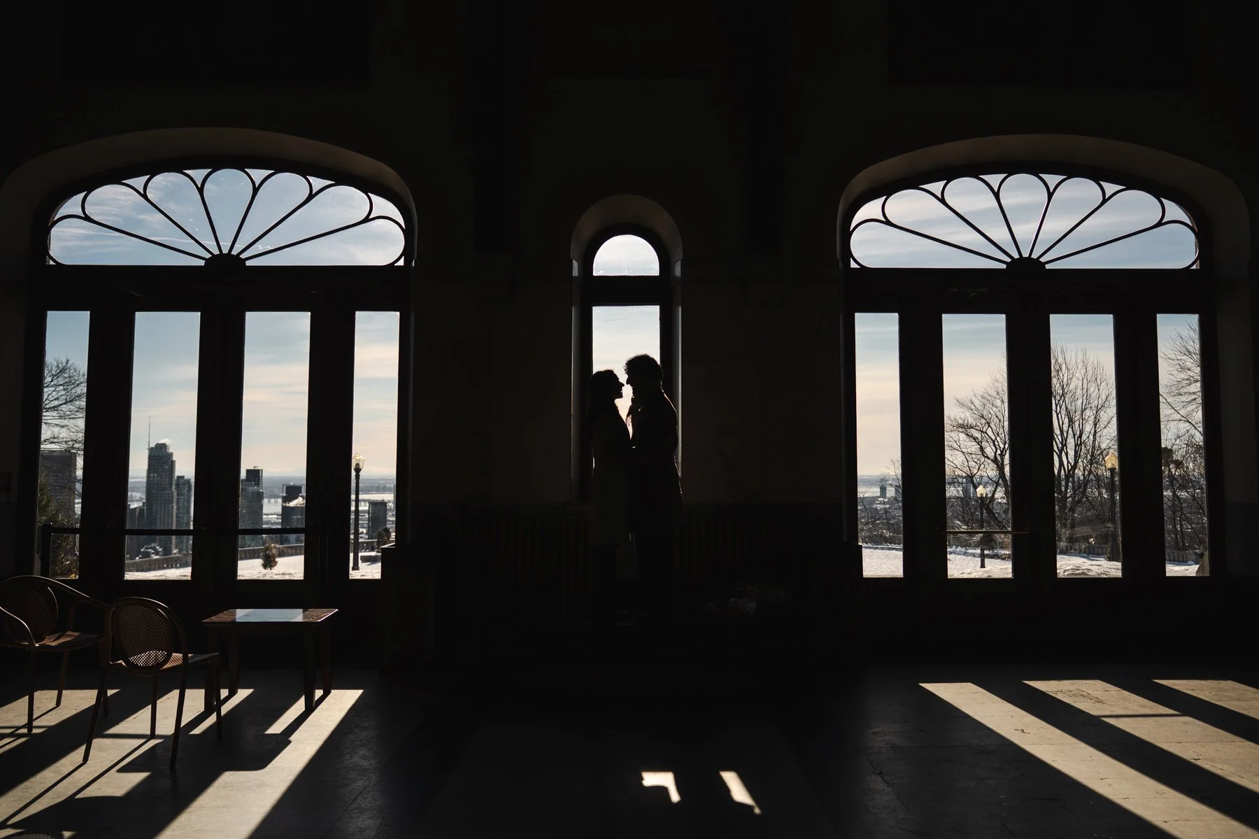 Silhouette of a man and woman staring into each other's eyes in a window, with a city backgrop behind outside.