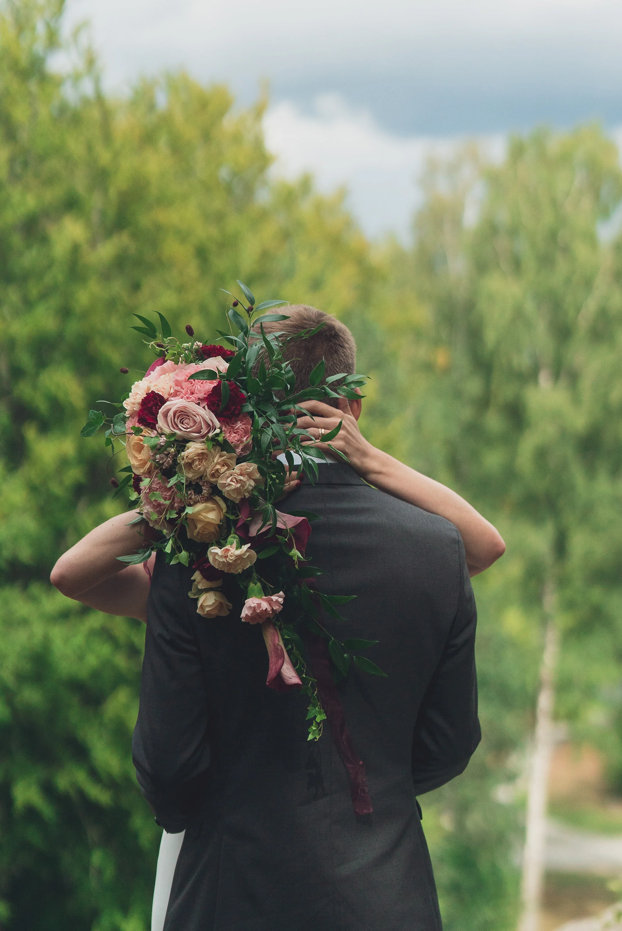 En person bär en stor bukett med blommor på ryggen medan de kysser sin partner i en grön park.