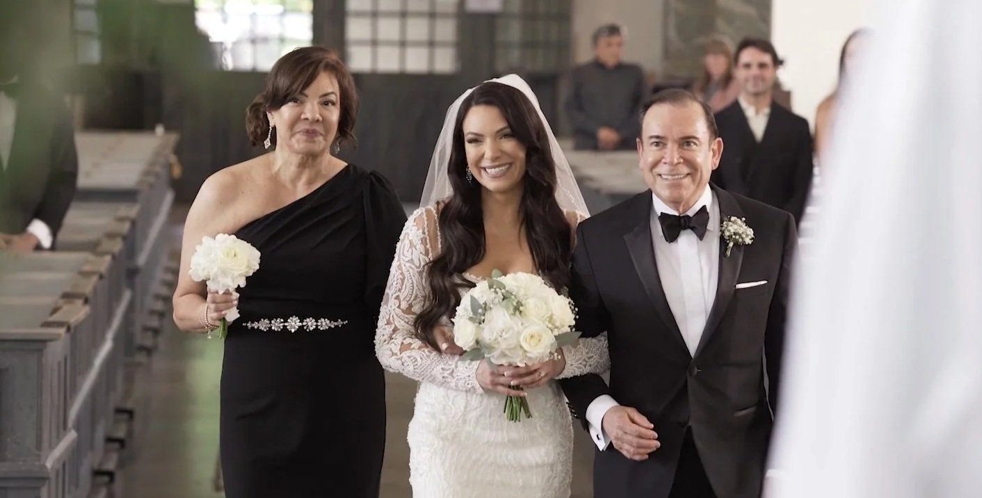 Bride walking down thi aisle together with her parents