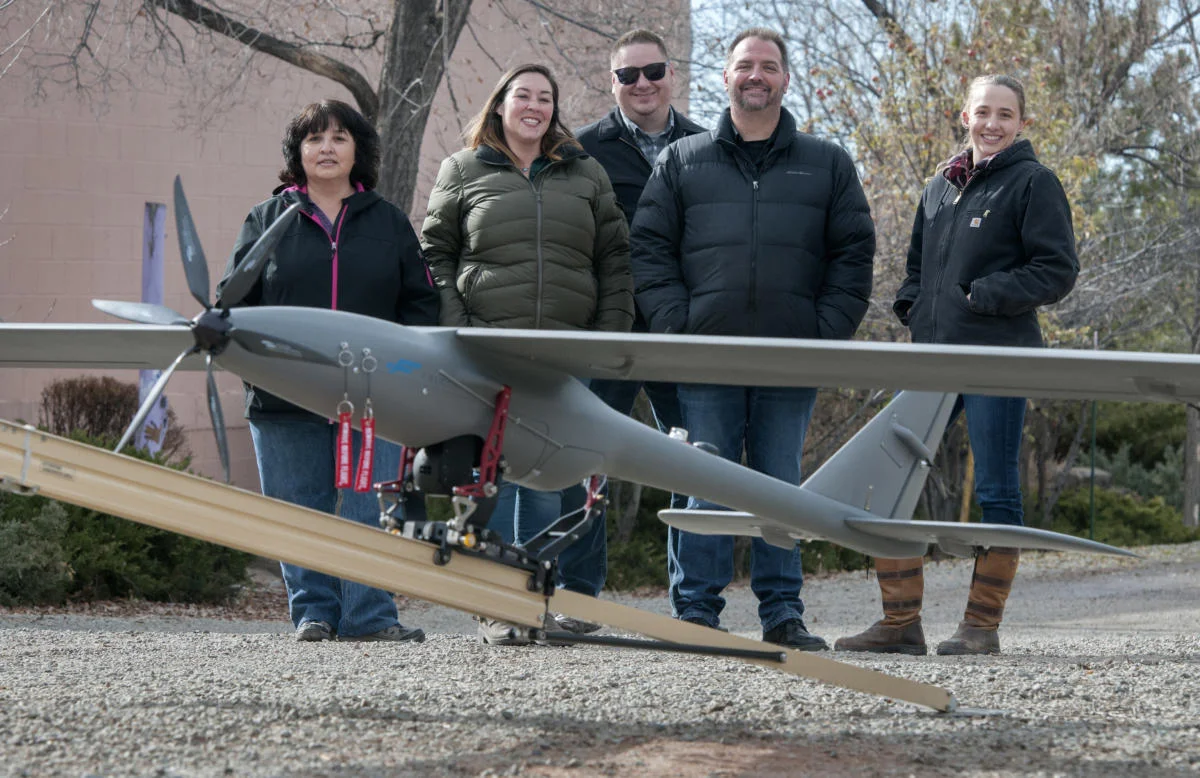 Wildflower International employees pose with their Silent Falcon drone at their office in Santa Fe. From left, Karen Sandoval, Laura Salazar, Michael Wahl, Rob Scism, all flight crew members, and Jenna deCastro the outside account executive for DOE. (Eddie Moore/Albuquerque Journal)