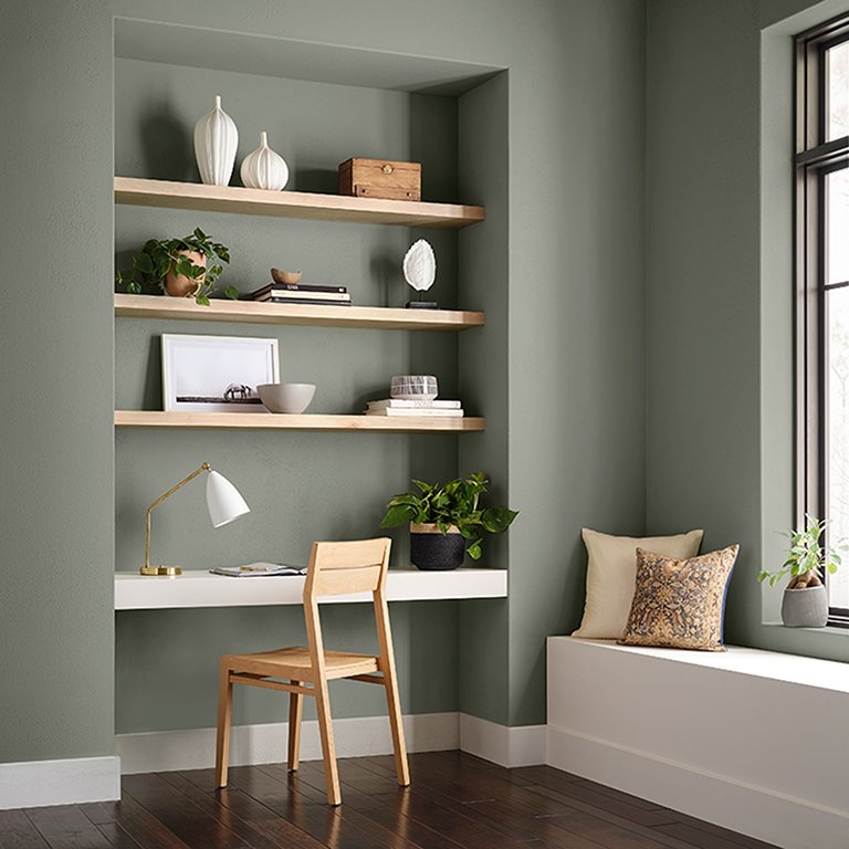  A minimalist office with floating wood shelves and Sherwin-Williams' 2022 Color of the Year, Evergreen Fog painted walls. 