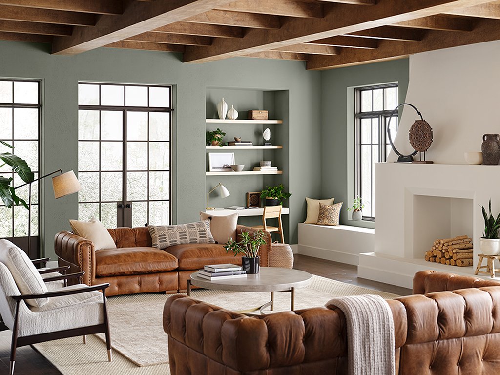  A living room, with a two leather couches, painted with Sherwin-Williams' 2022 Color of the Year, Evergreen Fog. 