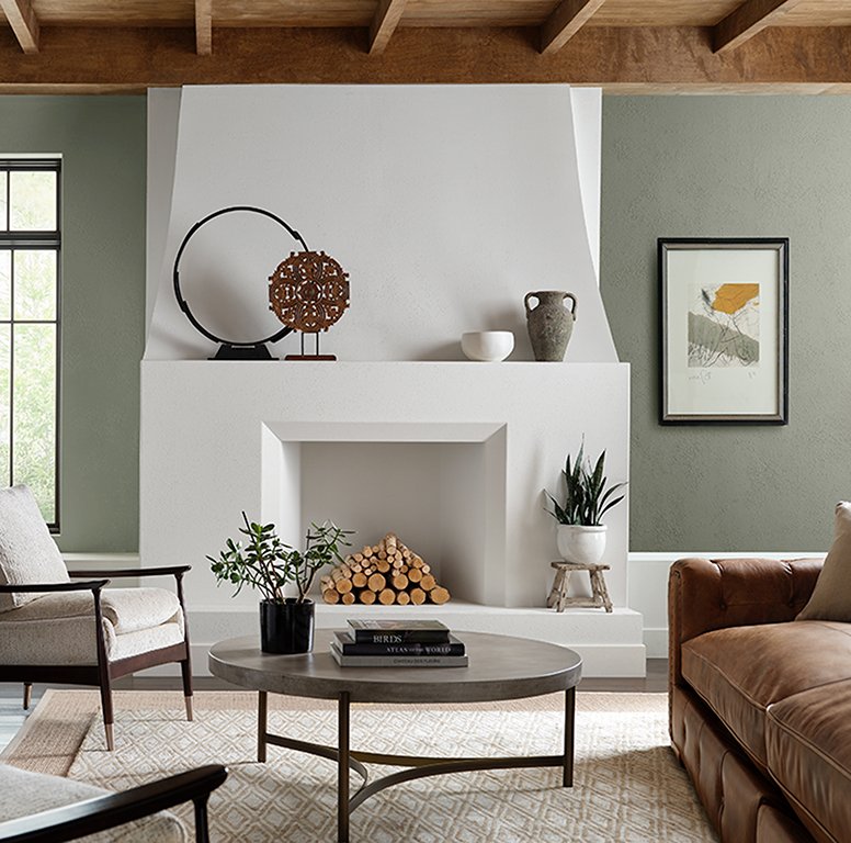  A modern white fireplace and coffee table framed by Evergreen Fog walls, Sherwin-Williams' 2022 Color of the Year. 