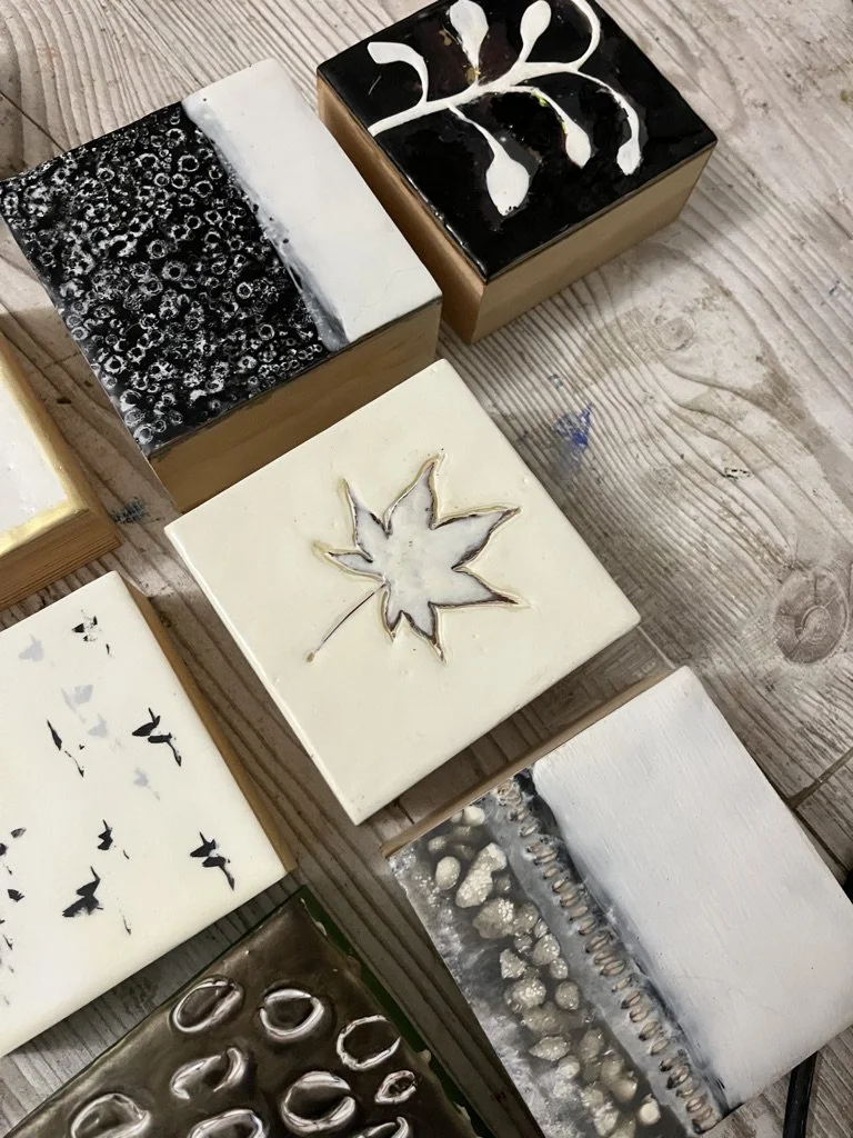 Various artistically decorated soap bars with black, white, gold, and silver designs, some with patterns such as bubbles, abstract swirls, a maple leaf, and butterflies, arranged on a wooden surface.