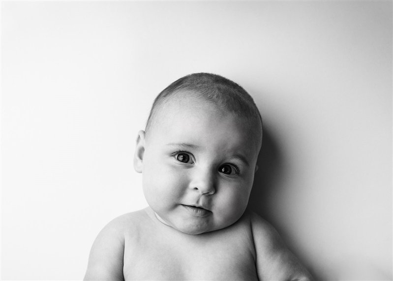 Black and white photo of a baby looking at the camera with a slight smile.