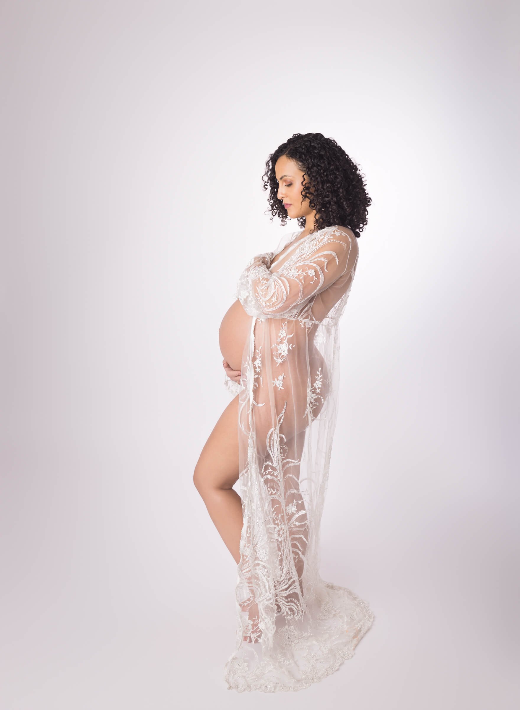 Pregnant woman wearing a sheer lace robe, standing in profile.