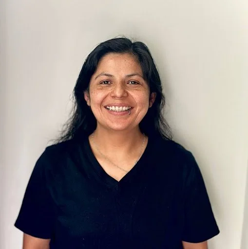 Mujer joven sonriendo viste una camiseta negra y está en un fondo blanco.
