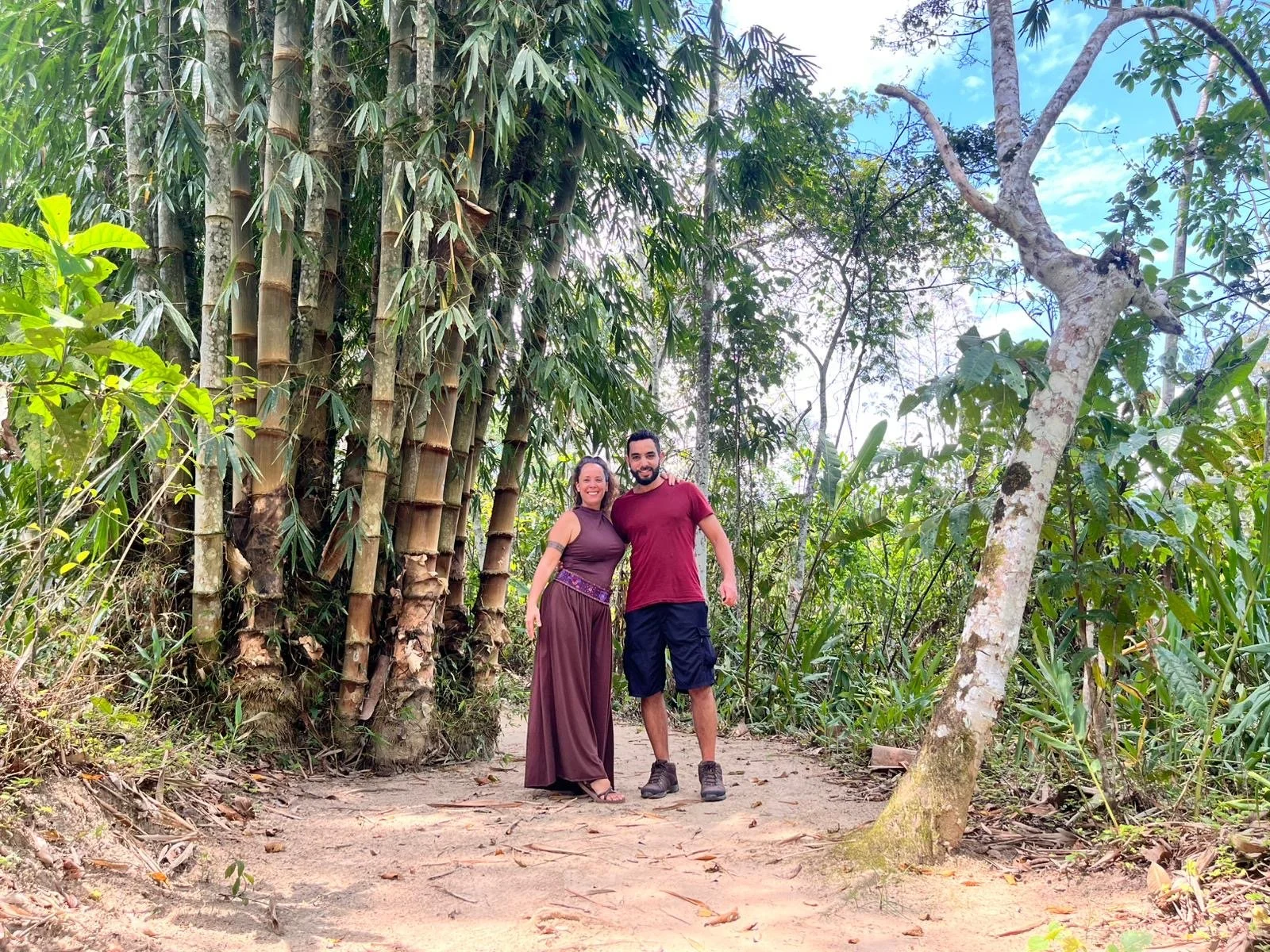 Dos personas sonrientes en un sendero rodeado de vegetación y árboles en un ambiente natural.
