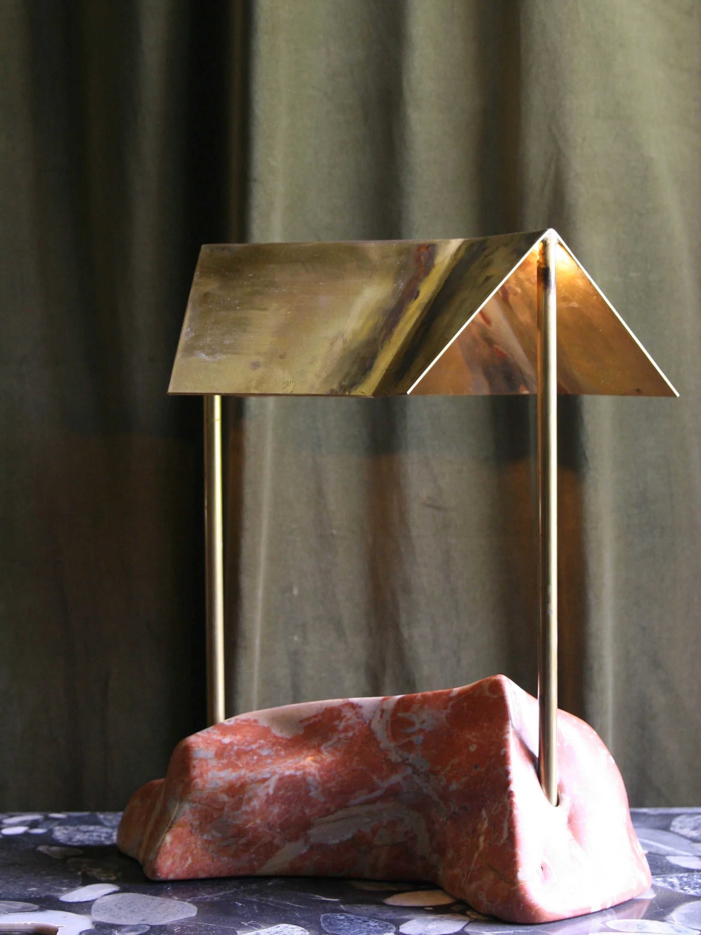 A decorative sculptural lamp featuring a pinkish marble base with gold and copper finish elements and black and white pebble pattern cloth underneath.