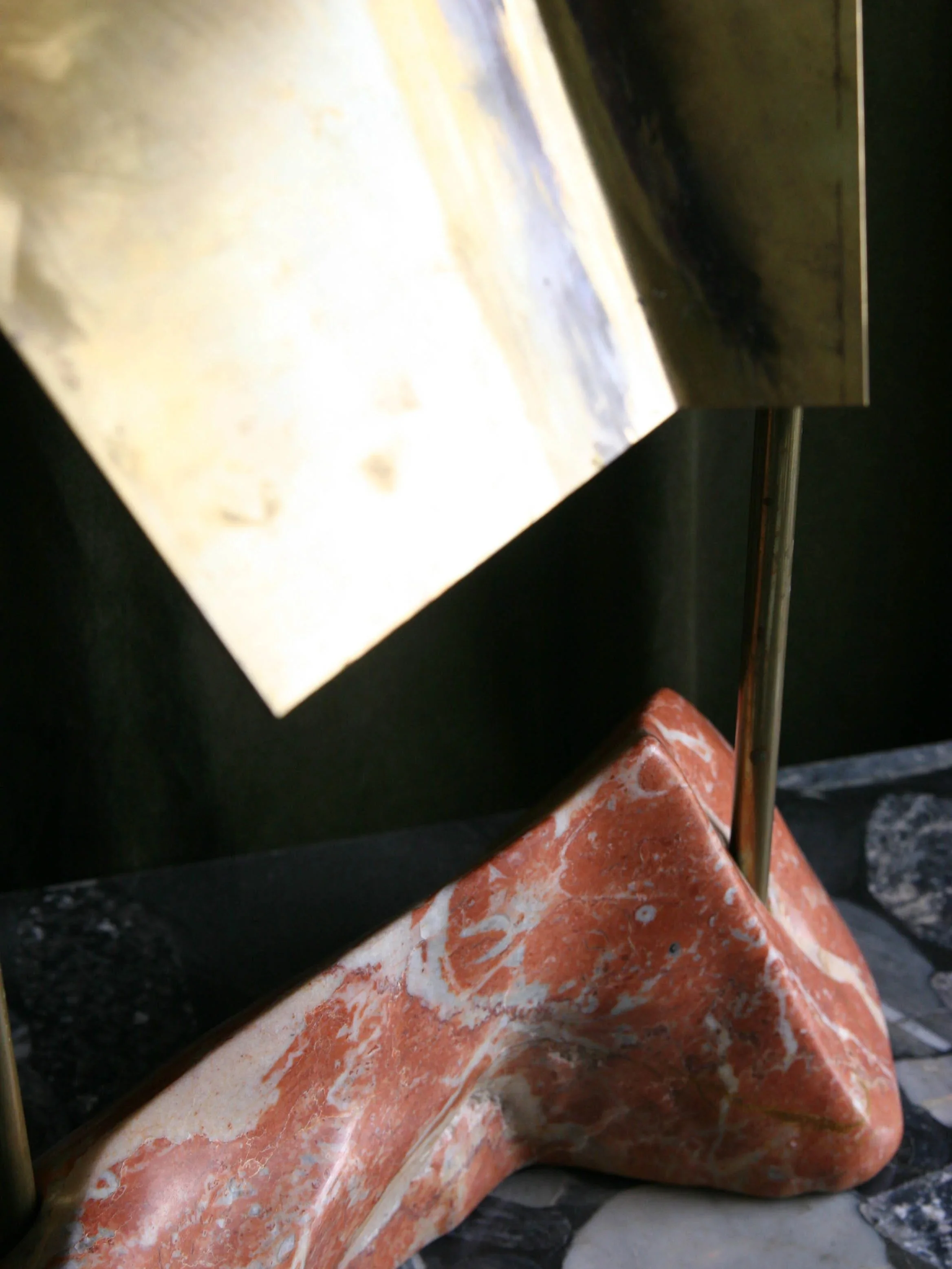 Close-up of a sculpture featuring a polished metal cube resting on a red marble base, with a black background.