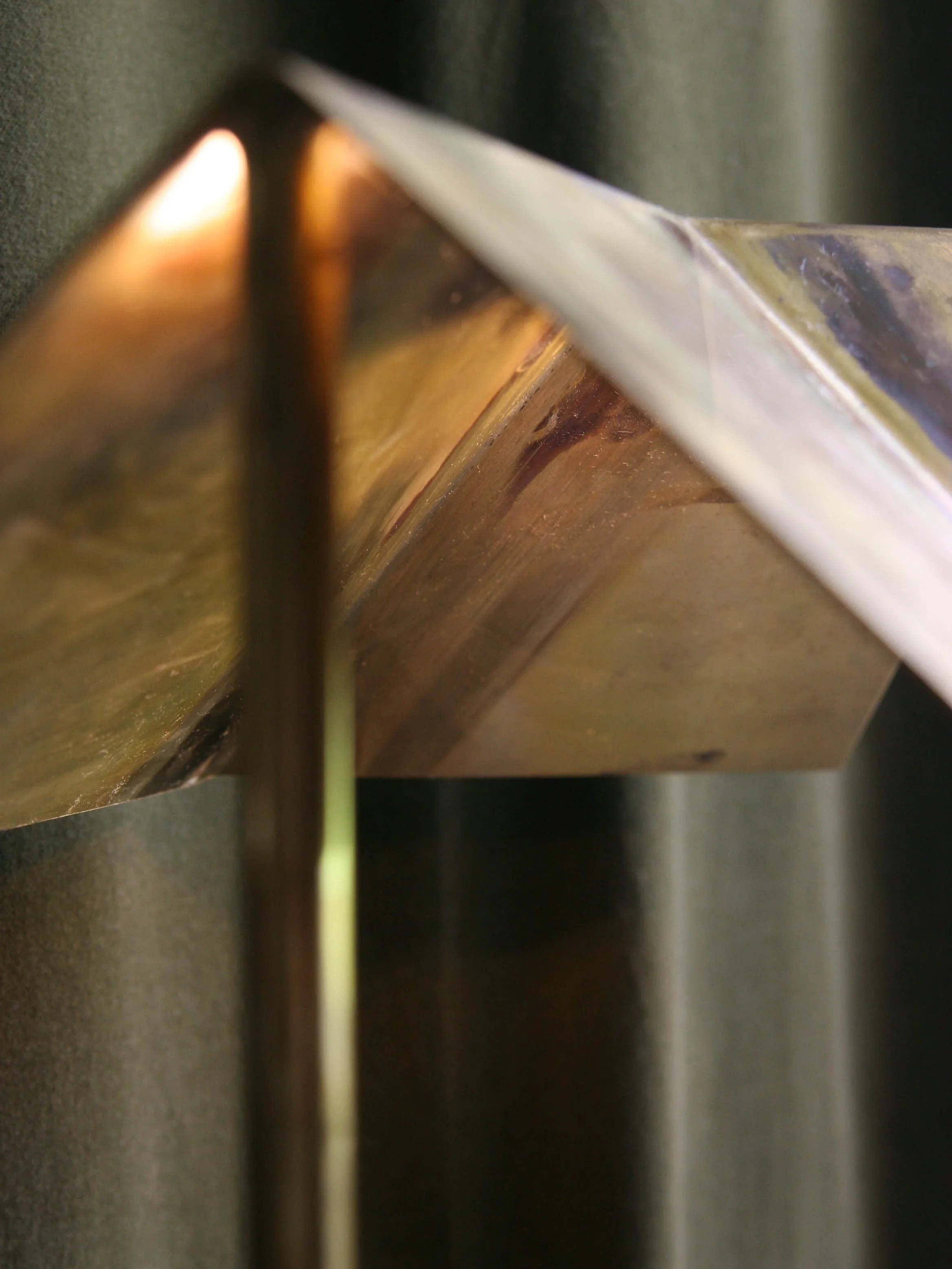 Close-up of a metallic object with a reflective surface, showing a diagonal edge and some reflections of warm light, with a dark background.