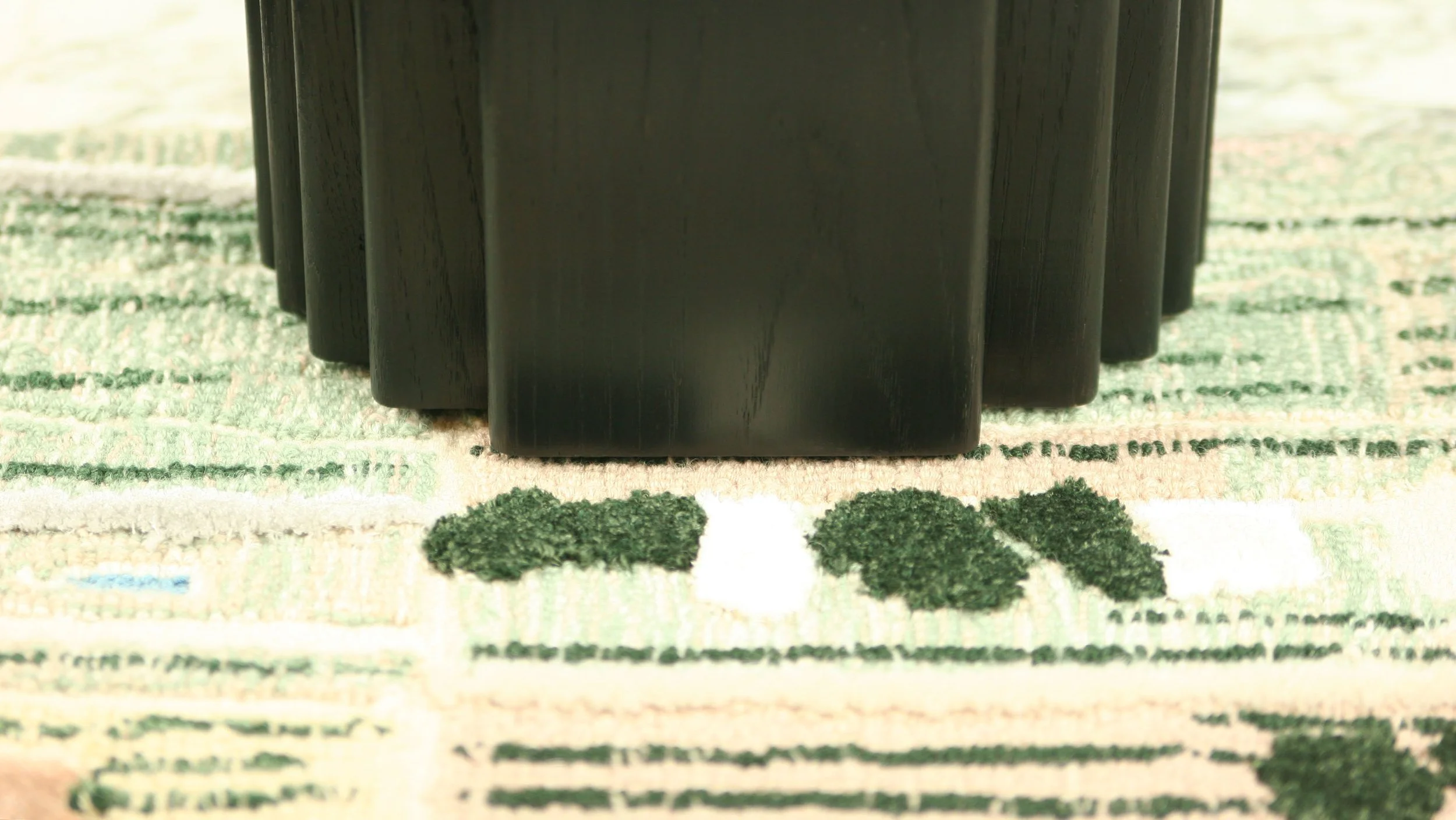 Detail view of EG-01 (Edge Occasional Side Table) base in blackened oak, made by Krzywda set on a Tangible Archives Epoch collection rug, designed by Edouard Sankowski, made in collaboration with Ateliers Pinton, showing loop pastels, green velvets