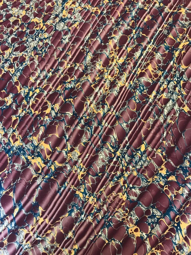 A sample of Jemma’s marbled papers in a maroon, gold, and navy blue ‘Spanish Ripple’ pattern.