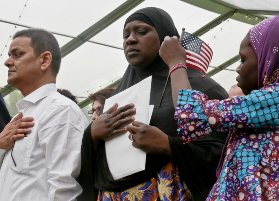 Fatoumata Jangana, center, stands for the National Anthem as her daughter fixes a miniature flag onto her hijab, during U.S. Citizen and Immigration Services ceremony for new citizens. (AP Photo/Bebeto Matthews)