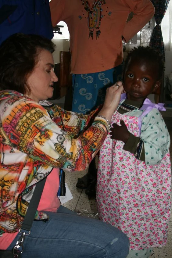 Arkansas children’s hospital Doctor, Dr. Lisa Buckmiller, assisting Kenyan child wearing one our divas dressing darlings dresses. This mission was in partnership with arkansas children’s hospital and the nonprofit, change of face.