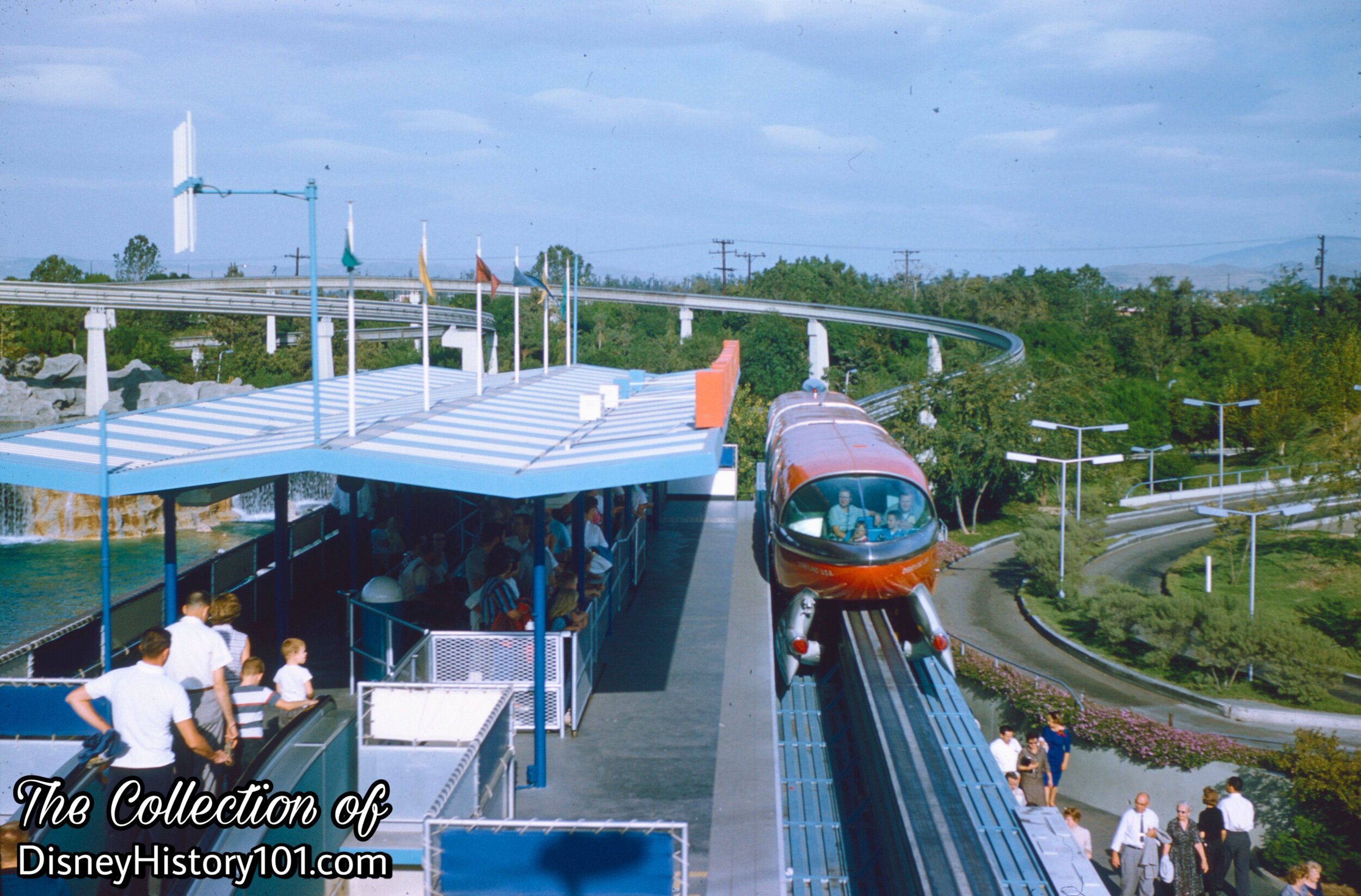 The tail cone of the Santa Fe & Disneyland - ALWEG Monorail Mark I Red at Tomorrowland Station (right) while Guests approach the Guest Control queue area (left).