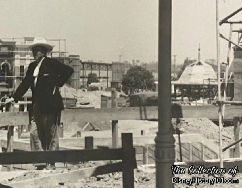 While Walt Disney stands framed by the covered waiting room of the Disneyland railroad station note the bandstand; World Wide Photo 6892-aje-6/9/55
