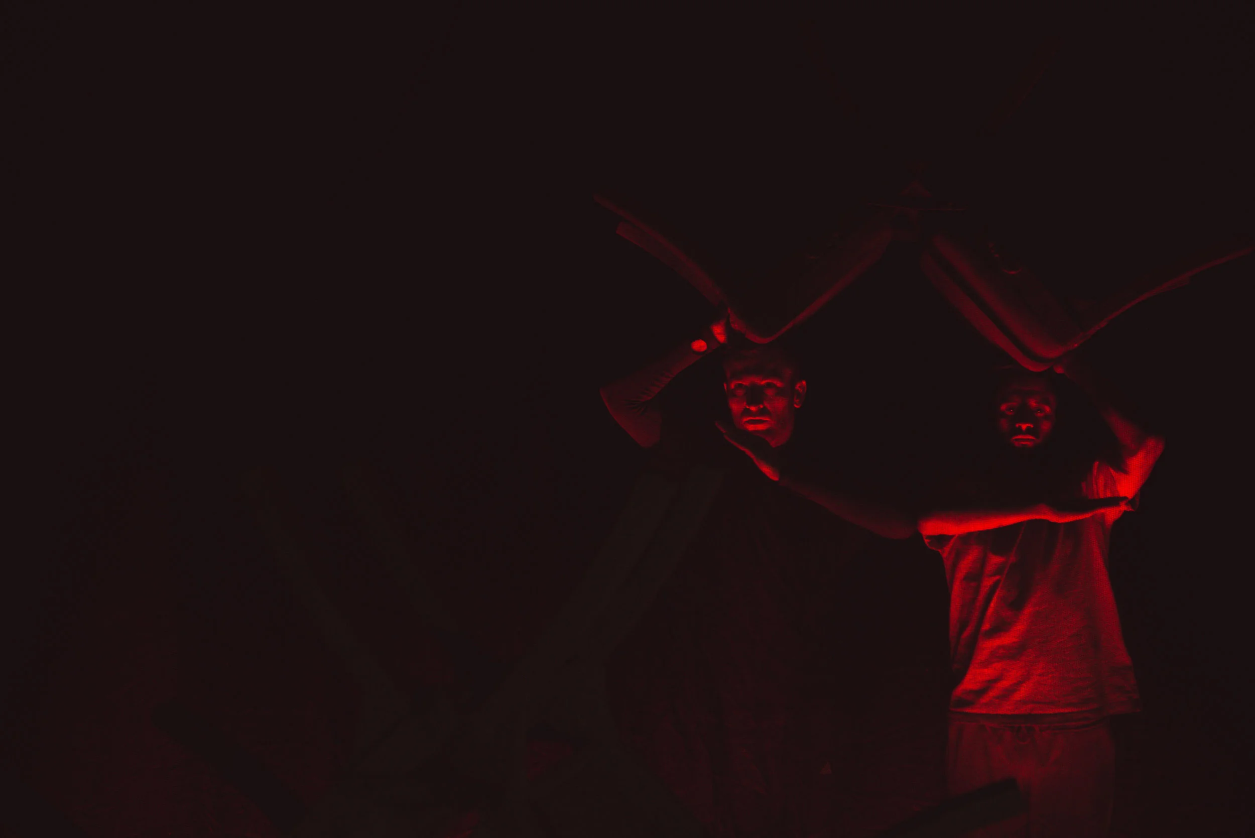 Deux personnes en vêtements sombres, portant des déguisements effrayants, avec un maquillage sombre, se tiennent dans une pièce sombre avec un éclairage rouge. L'une d'elles semble porter un masque ou un maquillage dramatique, créant une atmosphère inquiétante.