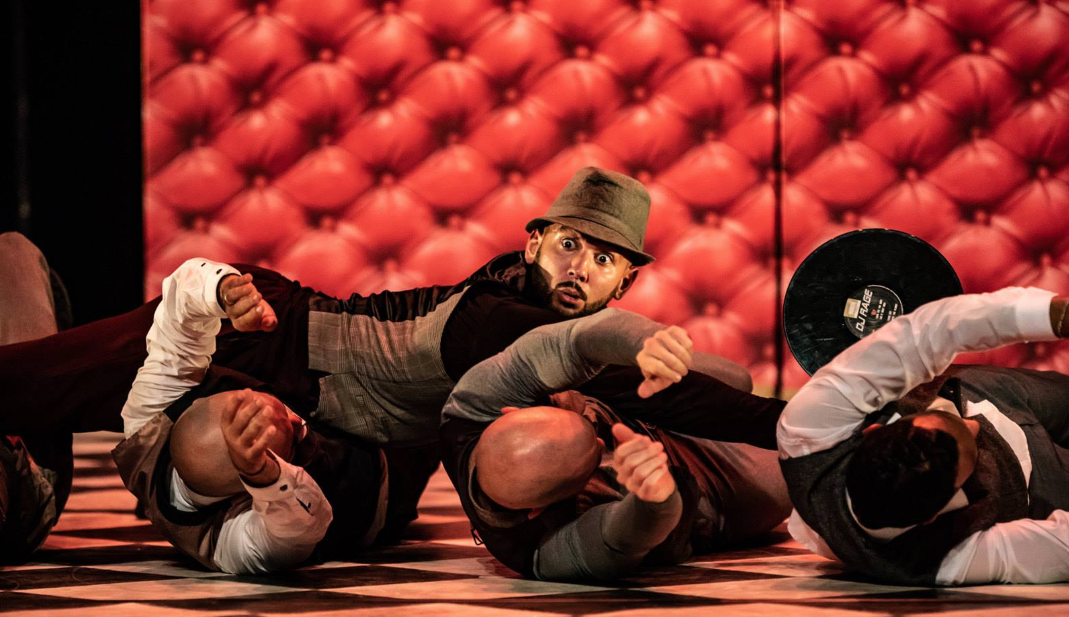 Un groupe de personnes en costume de MMA en train de faire un combat d'improvisation ou une scène d'arts martiaux sur scène avec un fond de tissu rouge capitonné.